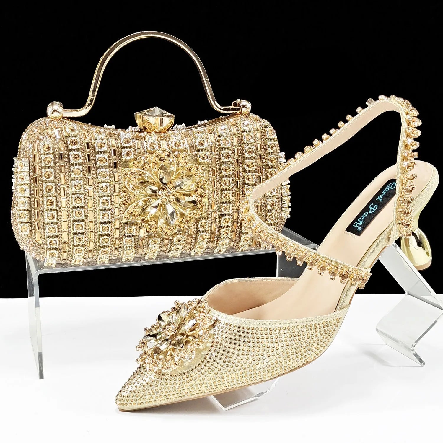 Women's black high heel sandals with ankle chain, floral rhinestone detail, and matching hard clutch bag