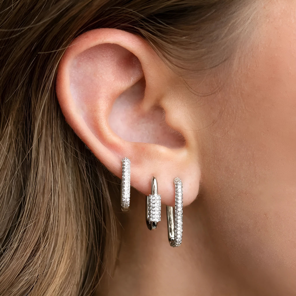 Three geometric square ear clips with inlaid zircon details in gold and white finishes on a grey background.