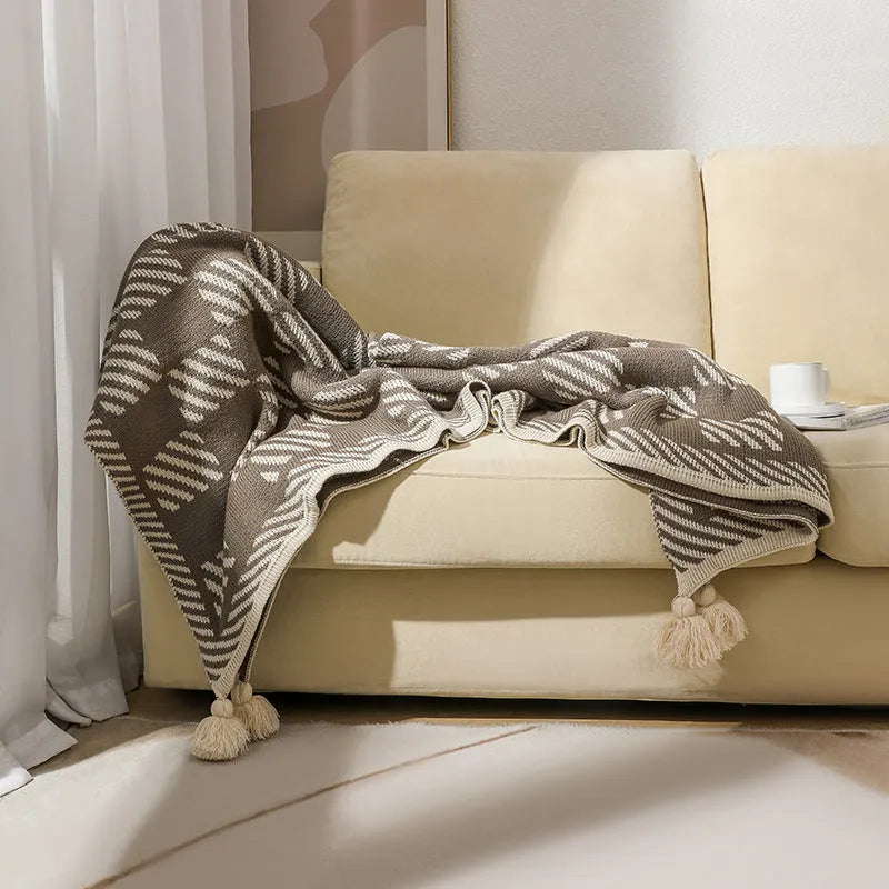 Beige and orange bohemian-style acrylic sofa blanket with tassel fringe on a grey sofa.