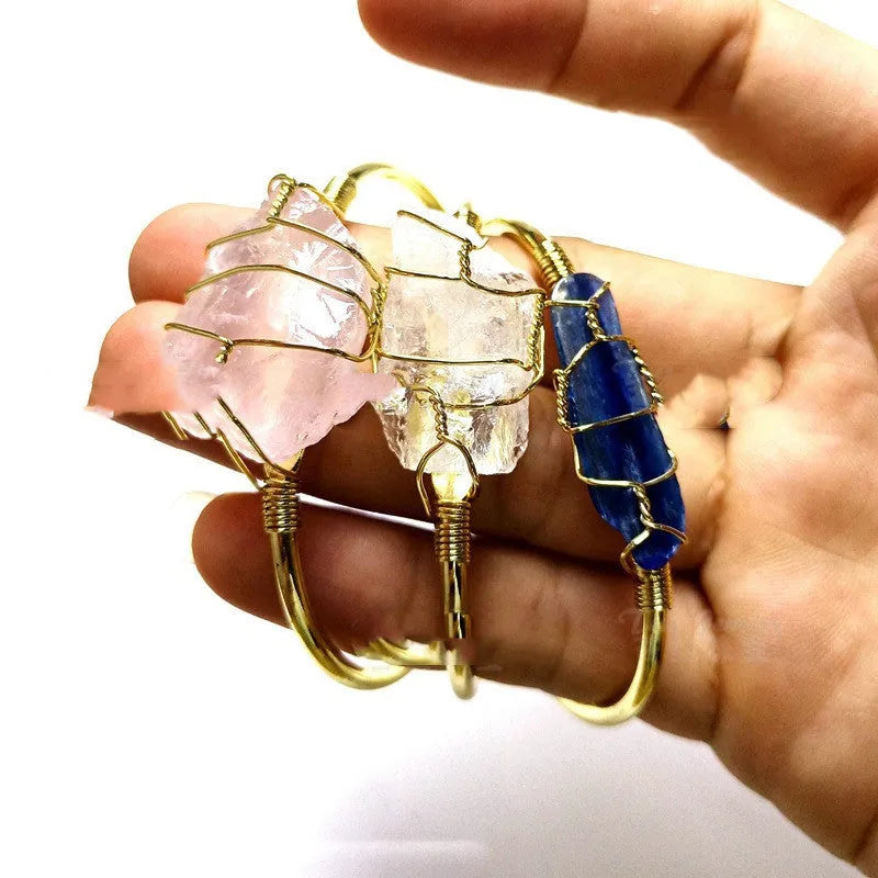 Gold winding geometric bracelet with unshaped rough natural crystal stones on a wrist.