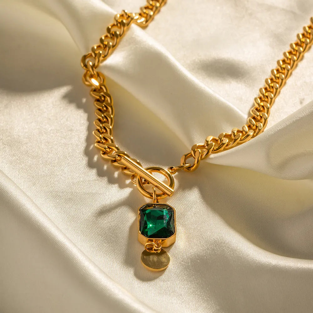 Gold electroplated titanium steel pendant necklace with geometric design and emerald zircon accents on Cuban link chain
