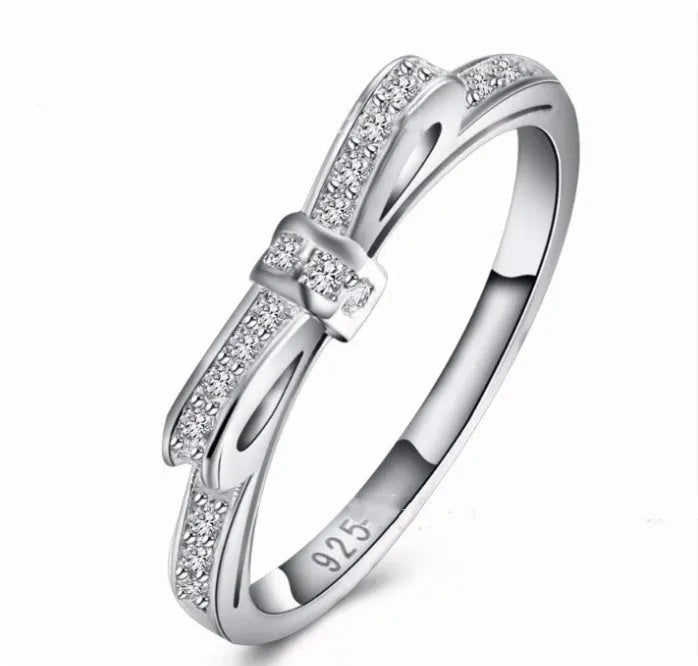 Silver coloured bow-shaped ring with sparkling rhinestone and zircon crystal details on a finger.