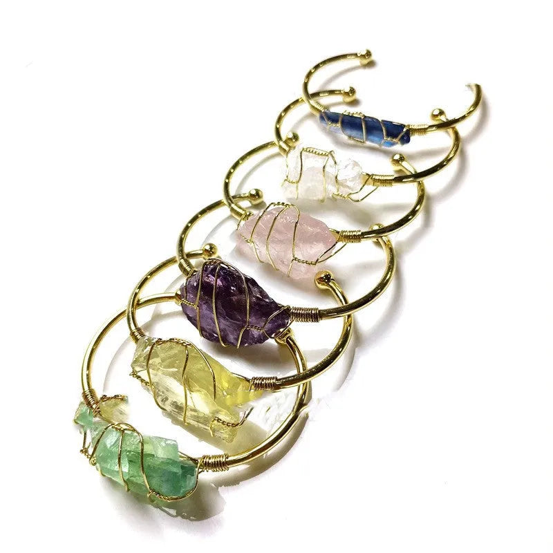 Gold winding geometric bracelet with unshaped rough natural crystal stones on a wrist.