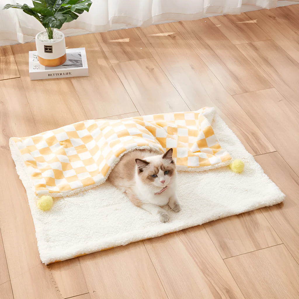 Green plaid pattern pet blanket with fur ball tassels on a sofa.