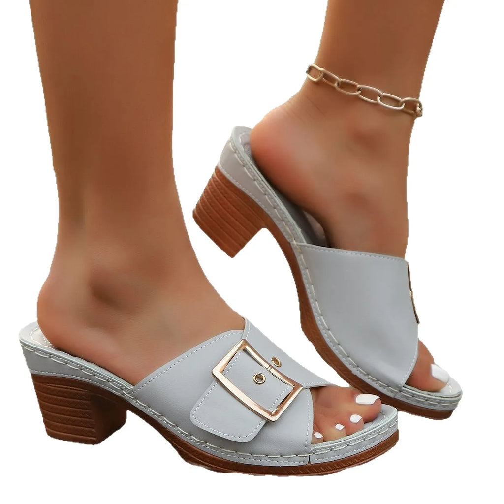 Women's black chunky heel slippers with a round toe and metal buckle on a light background.