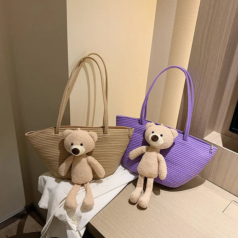 Large beige woven cotton linen shoulder bag with three-dimensional front pocket and double straps.