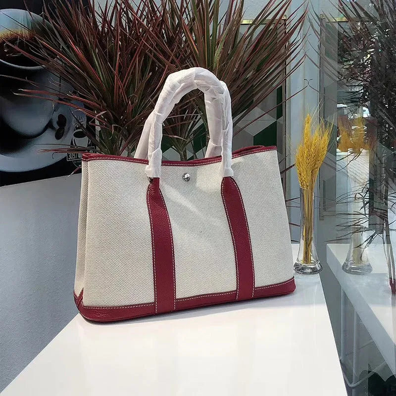 Women's canvas bucket tote bag with leather handles and detailing in black, shown with open top revealing internal zip pocket.
