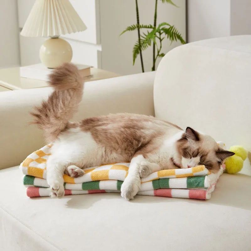 Green plaid pattern pet blanket with fur ball tassels on a sofa.