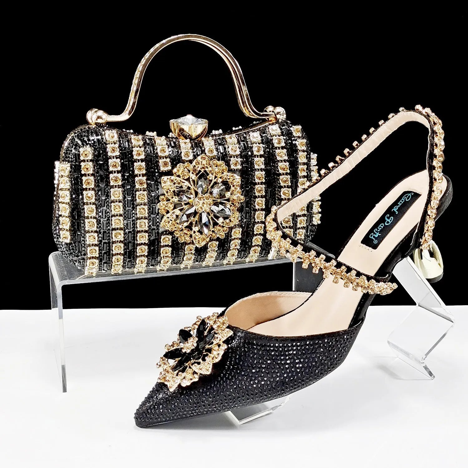 Women's black high heel sandals with ankle chain, floral rhinestone detail, and matching hard clutch bag