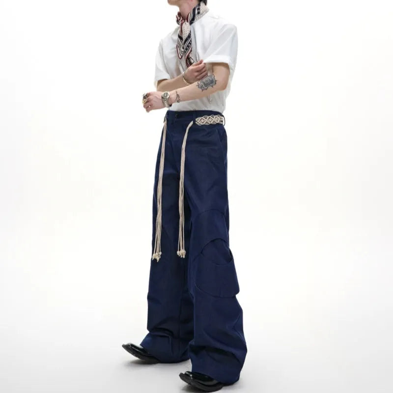 Men's dark blue straight-leg jeans with heavy 3D cutting, showing zipper decoration and tassel detail on a loose fit.