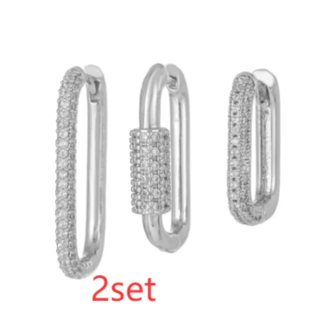 Three geometric square ear clips with inlaid zircon details in gold and white finishes on a grey background.