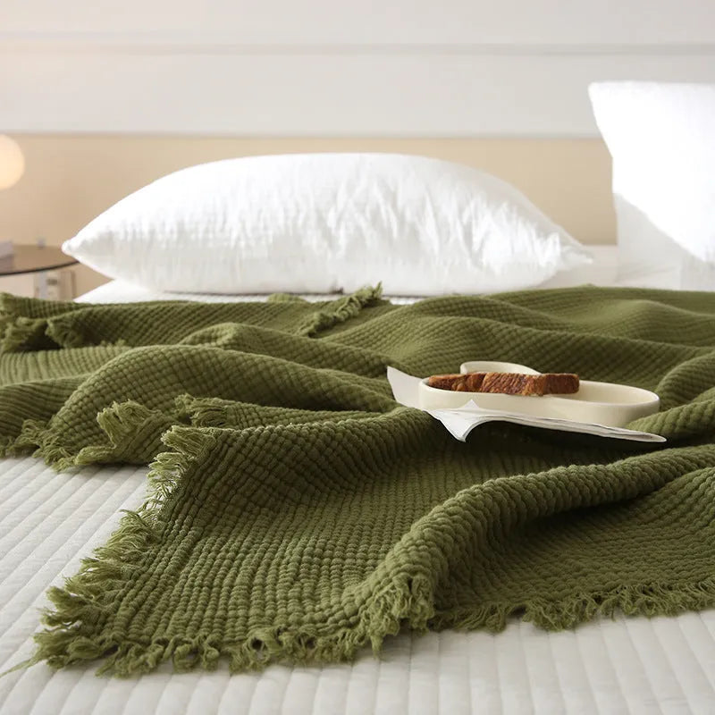 Four-layer gauze cotton tassel blanket in avocado green colour laid flat.