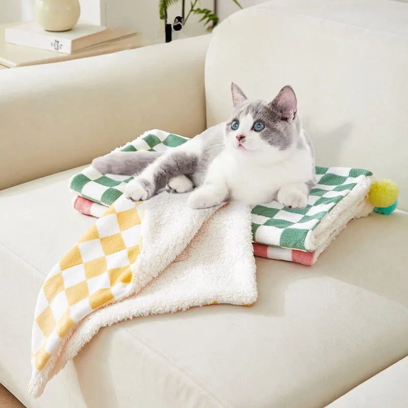 Green plaid pattern pet blanket with fur ball tassels on a sofa.