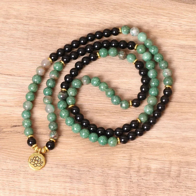 Green and black elastic beaded bracelet with metallic alloy charm details on a wrist.