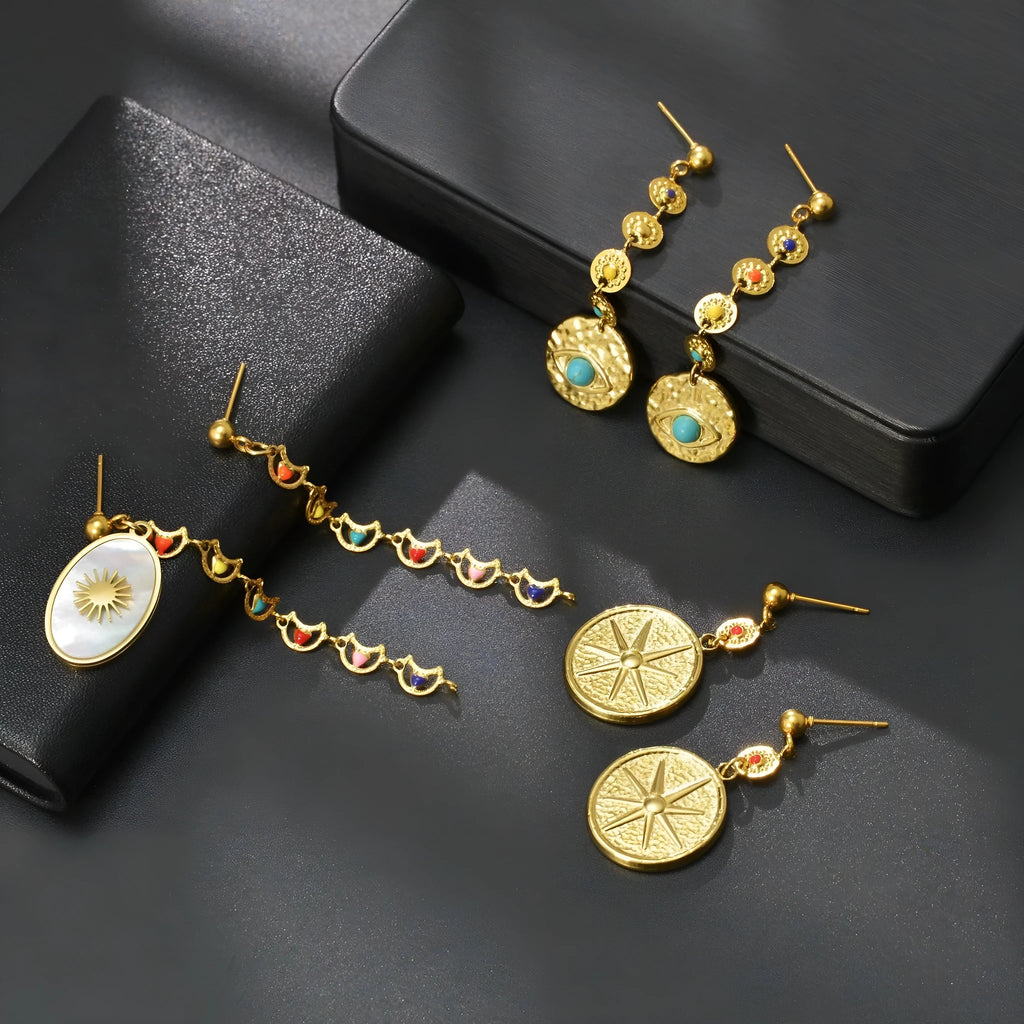 Stainless steel geometric drop earrings showing eight-awn star, eye, and shell sun designs in silver tone