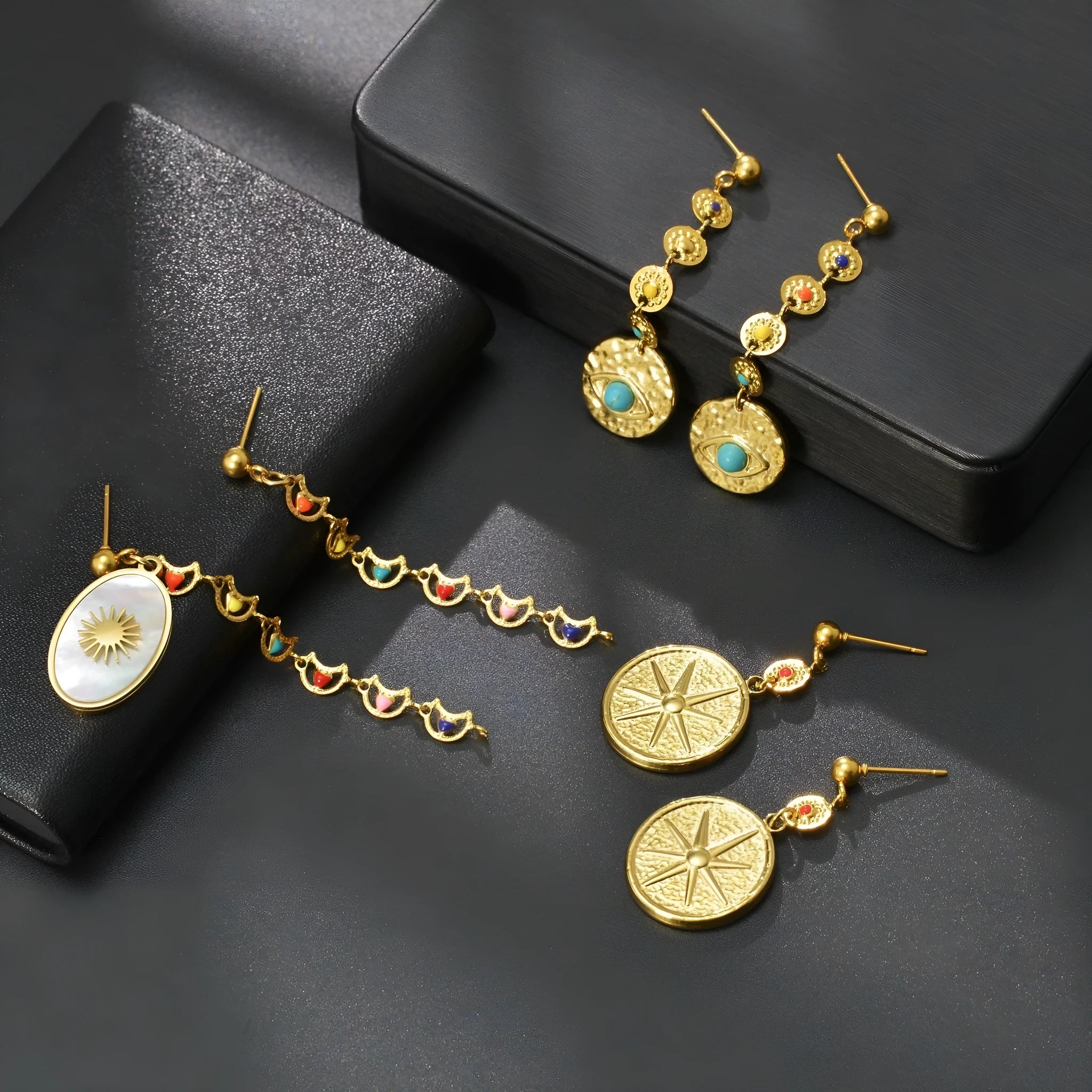 Stainless steel geometric drop earrings showing eight-awn star, eye, and shell sun designs in silver tone