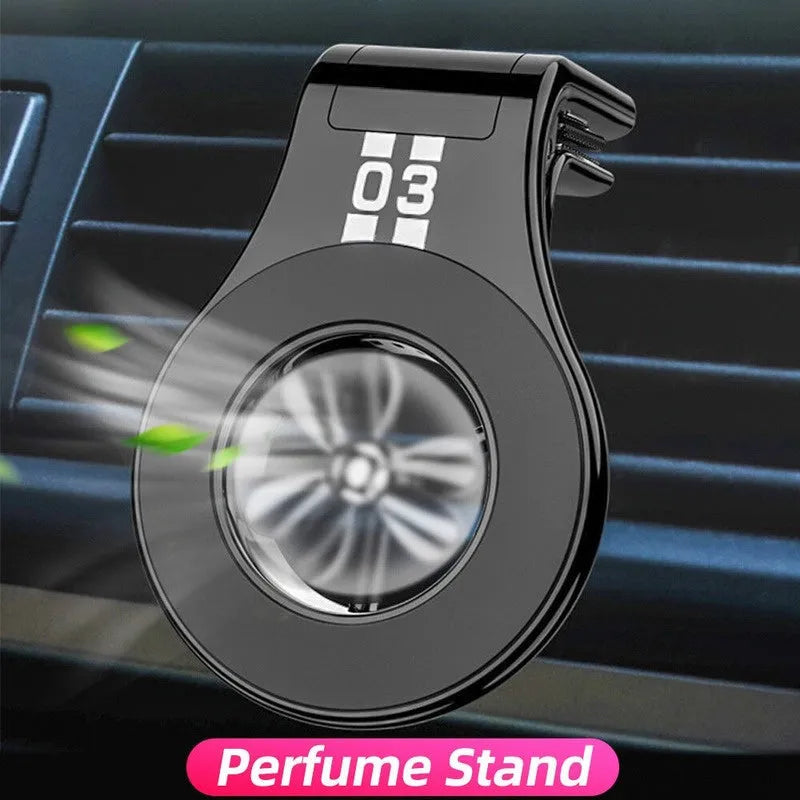 Black magnetic car phone holder clipped to a car air vent, showing a smartphone attached and the included fragrance slice.