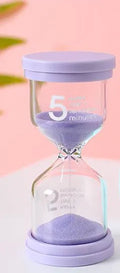 Handmade glass sand clock timer on a desk, showing purple sand, modern design.