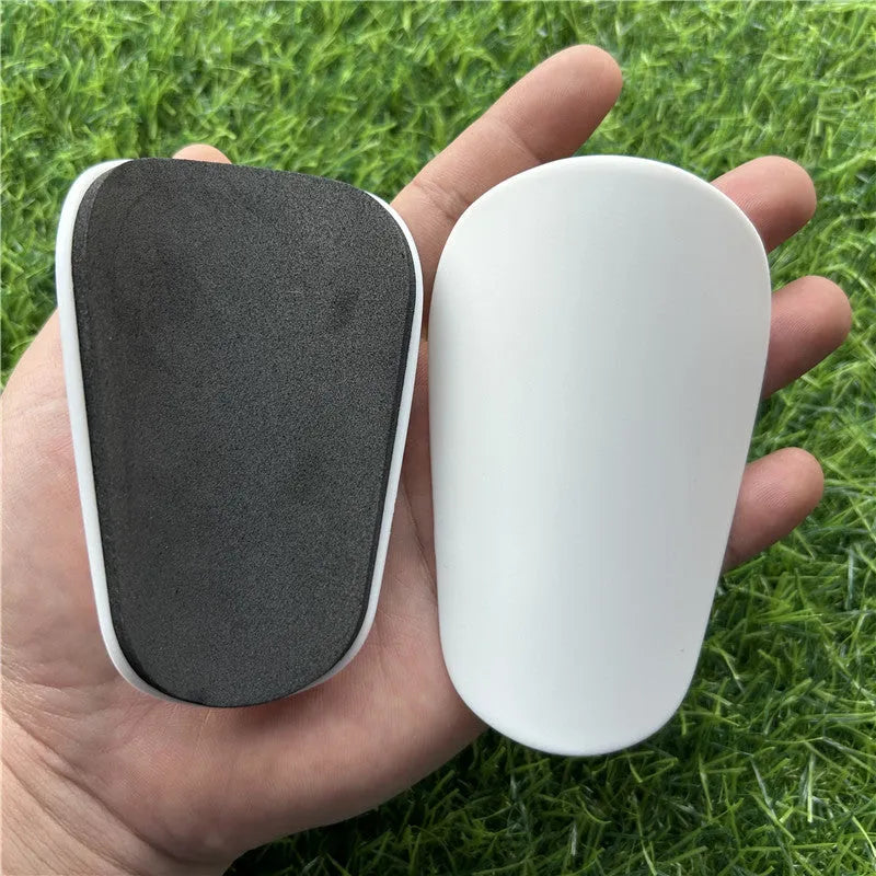Extra small black and white plastic football shin guards measuring 8x5cm and 10x6cm