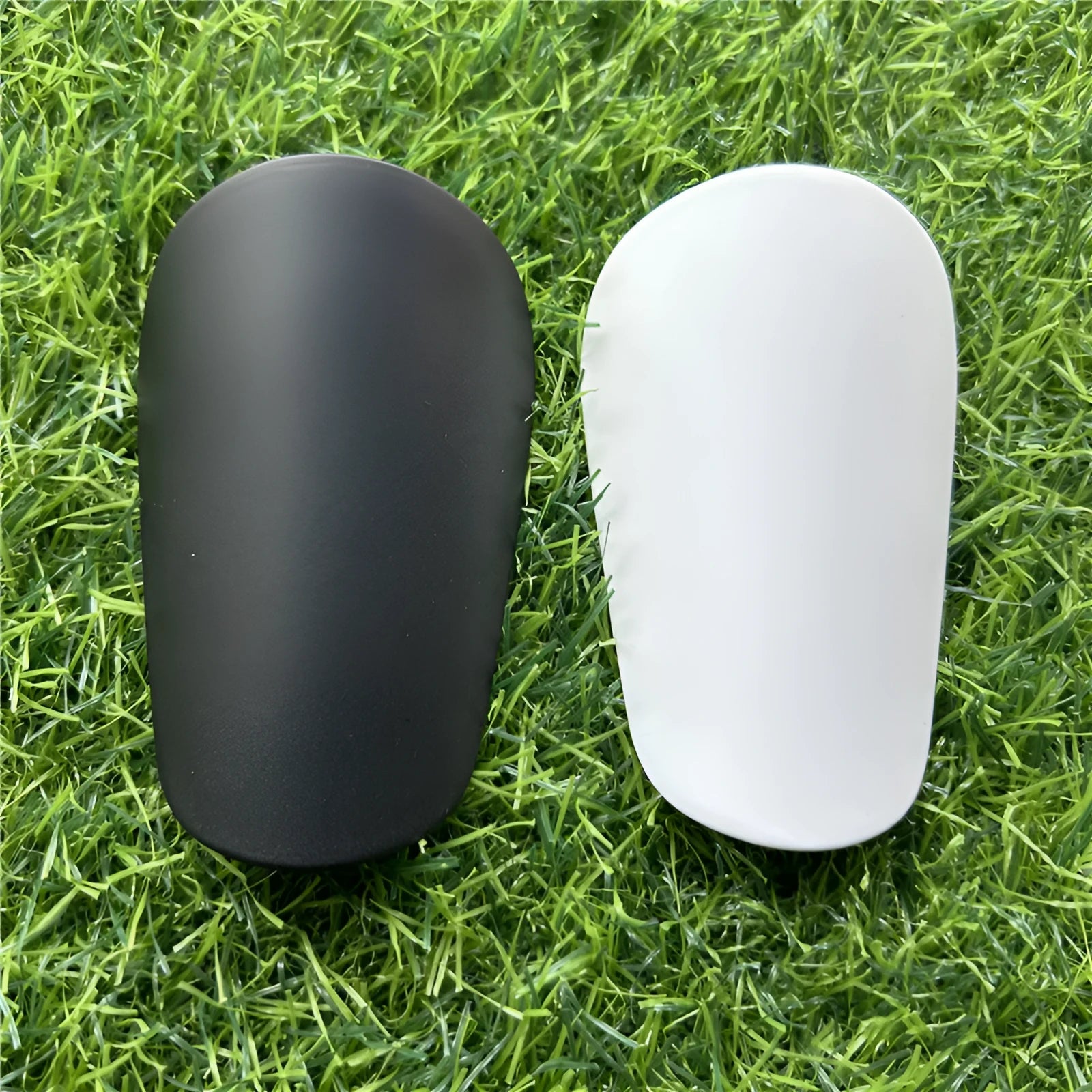 Extra small black and white plastic football shin guards measuring 8x5cm and 10x6cm