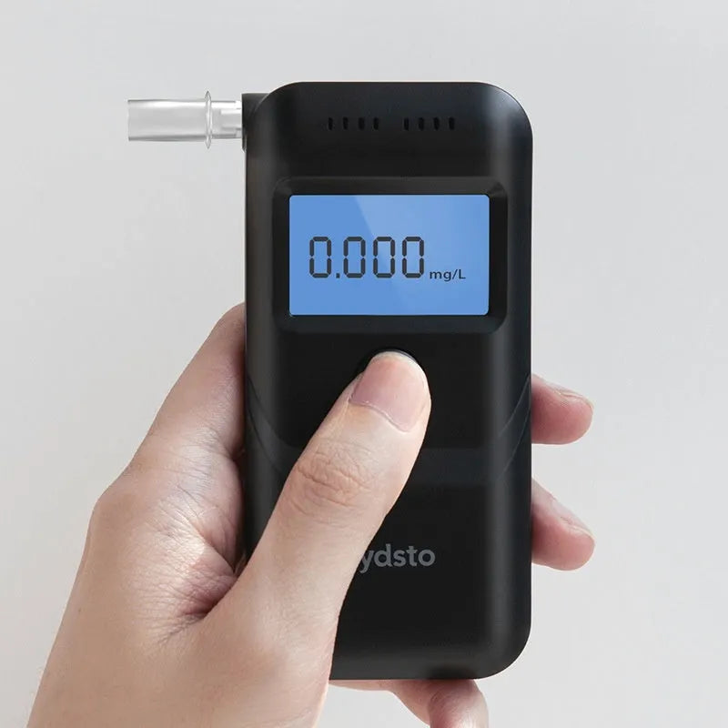 Black portable household alcohol breath tester with LCD screen on a dark background.
