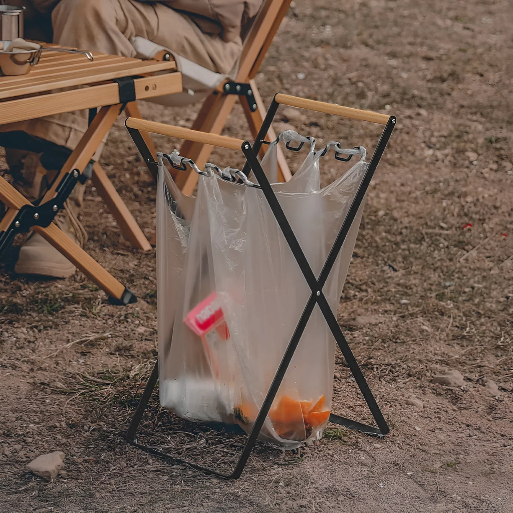 Black iron folding storage rack with a wooden handle for hanging outdoor waste bags.