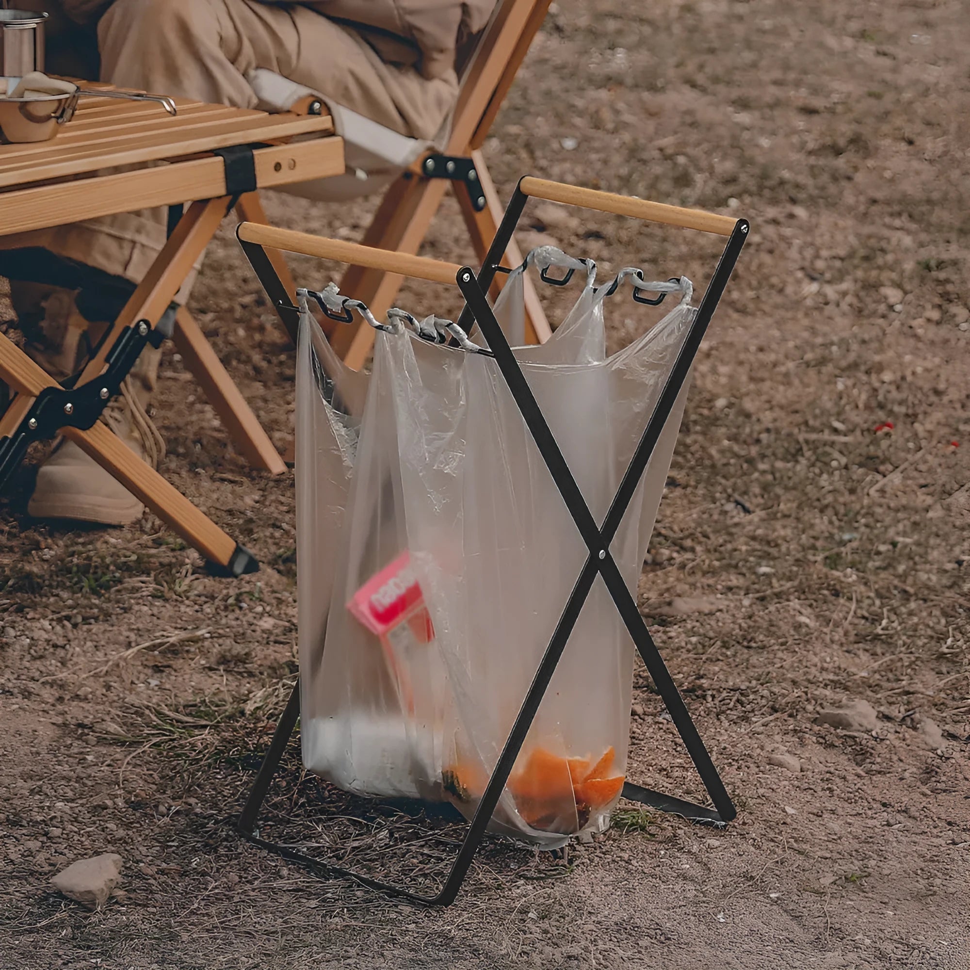 Black iron folding storage rack with a wooden handle for hanging outdoor waste bags.