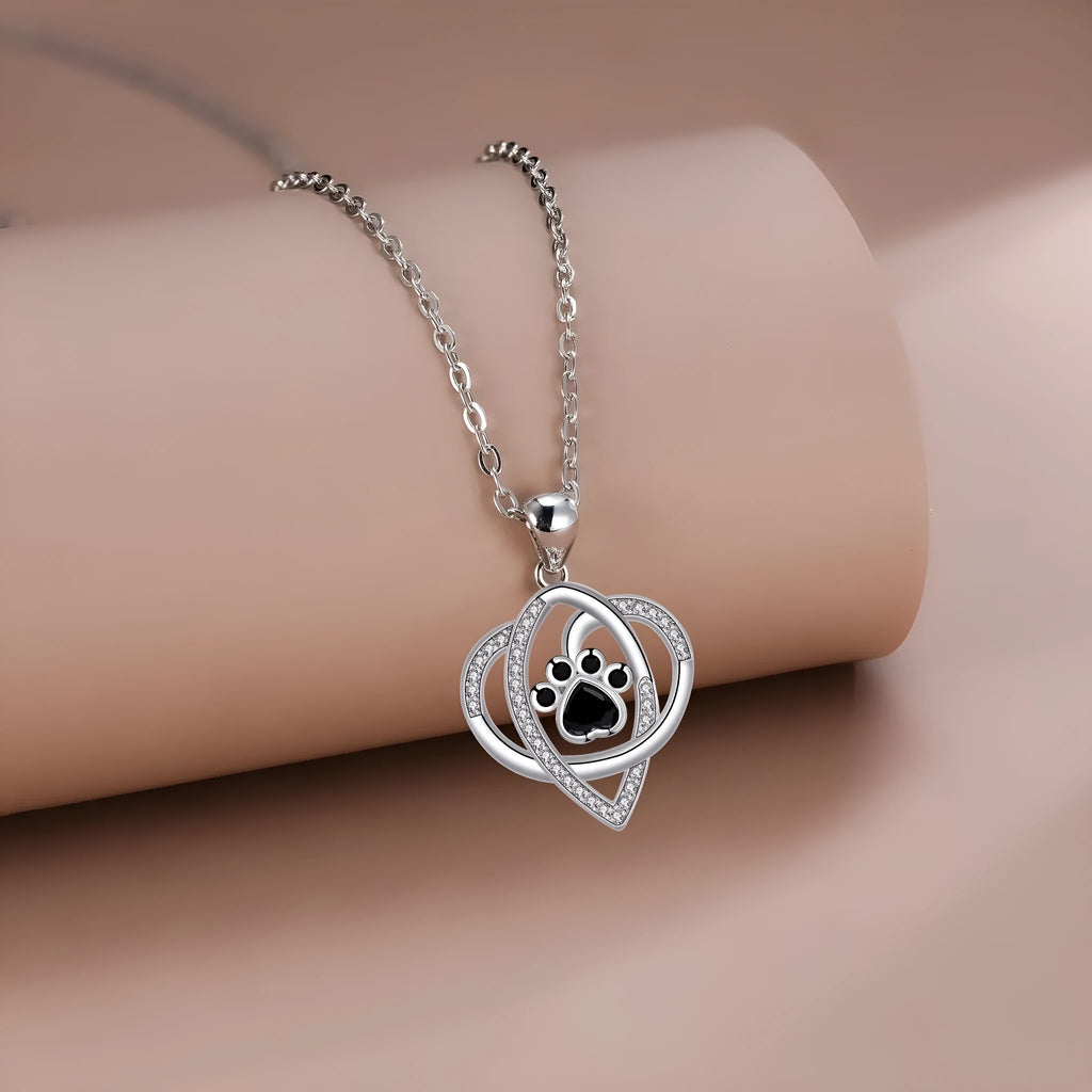 Close-up of a copper necklace pendant showing detailed dog and cat paw prints on a cross chain.