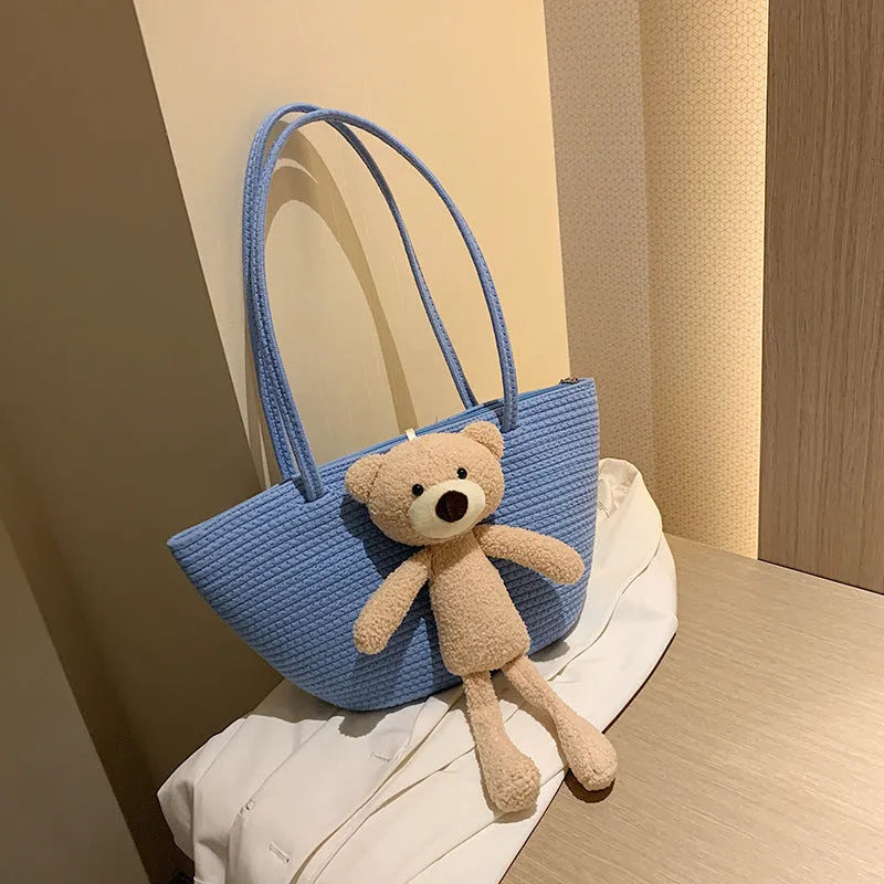 Large beige woven cotton linen shoulder bag with three-dimensional front pocket and double straps.