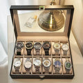 Grey leather watch storage box with transparent lid showing multiple watch slots inside