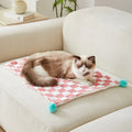 Green plaid pattern pet blanket with fur ball tassels on a sofa.
