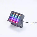 Silver aluminium outdoor LED spotlight projecting multi-coloured light onto trees.