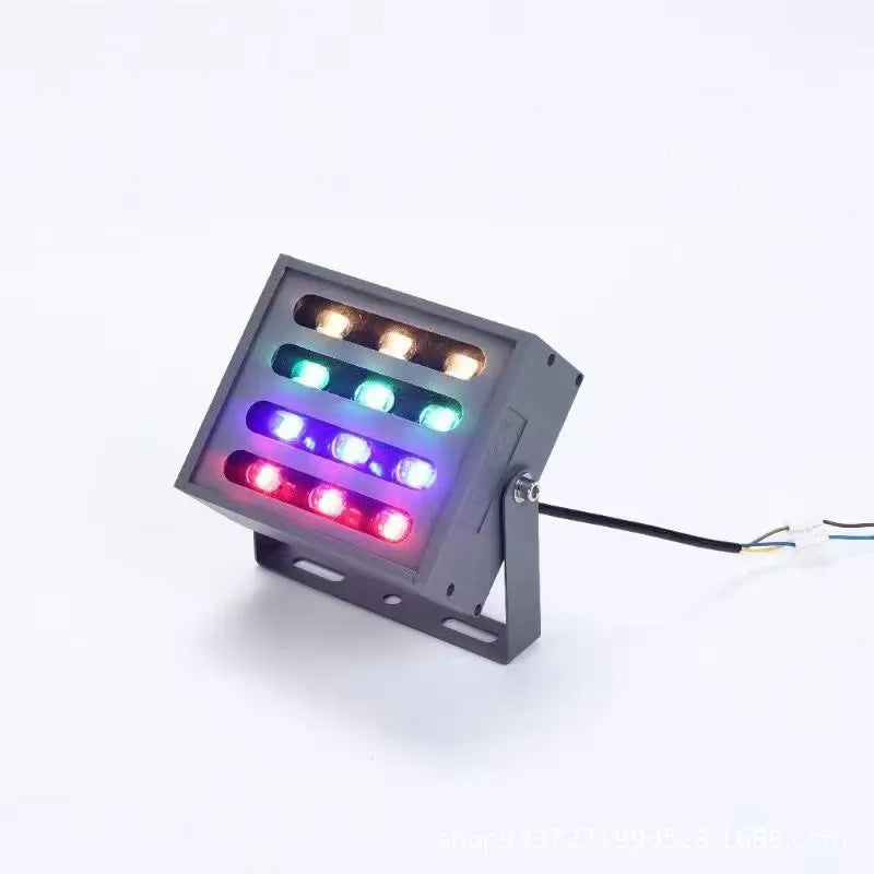 Silver aluminium outdoor LED spotlight projecting multi-coloured light onto trees.