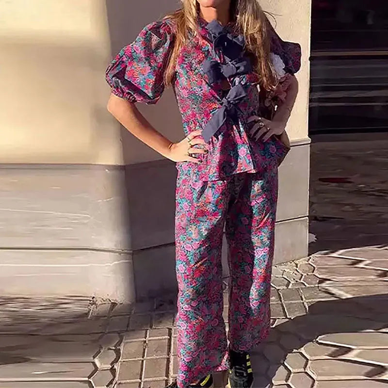 Women's floral print two-piece suit with a tie-neck puff sleeve top and matching trousers.