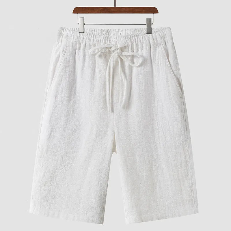 Men's beige linen casual shorts with loose cropped fit and elastic waistband laid flat