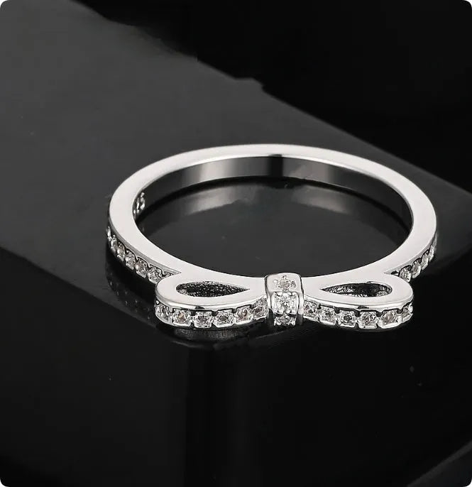 Silver coloured bow-shaped ring with sparkling rhinestone and zircon crystal details on a finger.