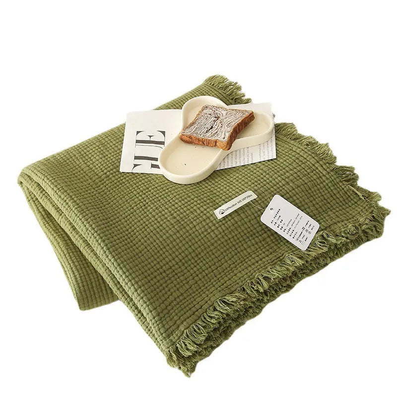 Four-layer gauze cotton tassel blanket in avocado green colour laid flat.