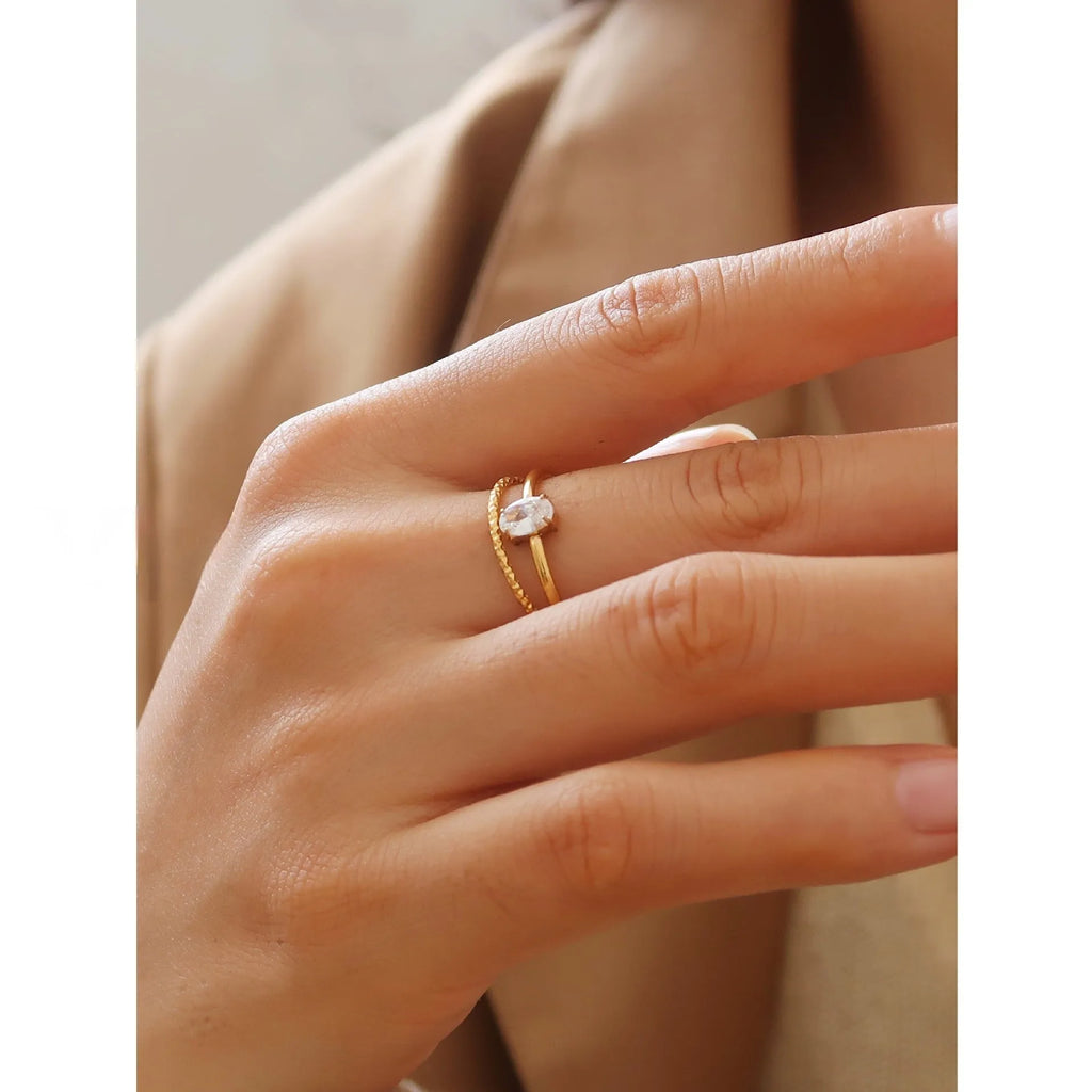 Golden electroplated stainless steel love heart ring and oval ring for women on a plain background.