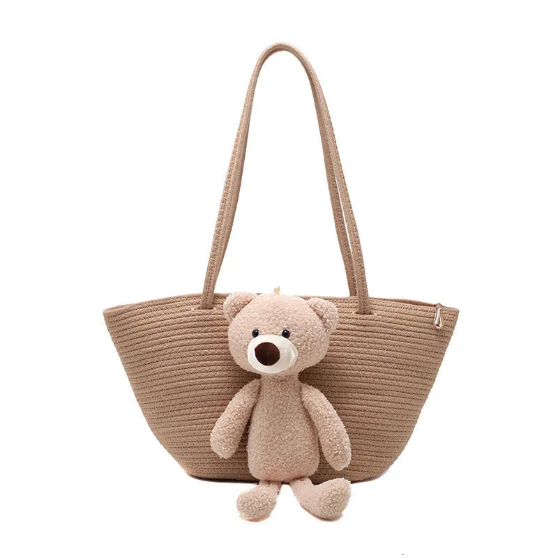 Large beige woven cotton linen shoulder bag with three-dimensional front pocket and double straps.