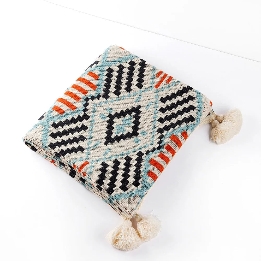 Beige and orange bohemian-style acrylic sofa blanket with tassel fringe on a grey sofa.