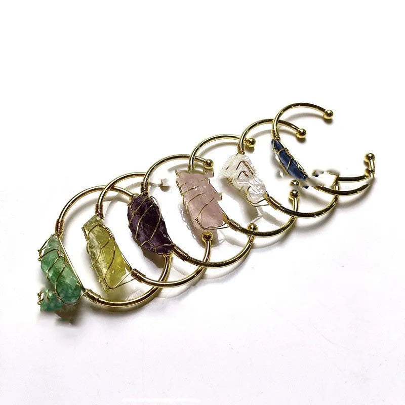 Gold winding geometric bracelet with unshaped rough natural crystal stones on a wrist.
