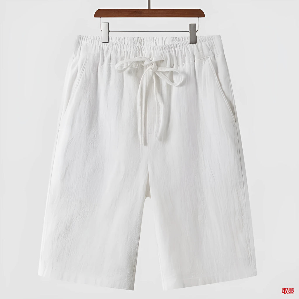 Men's beige linen casual shorts with loose cropped fit and elastic waistband laid flat