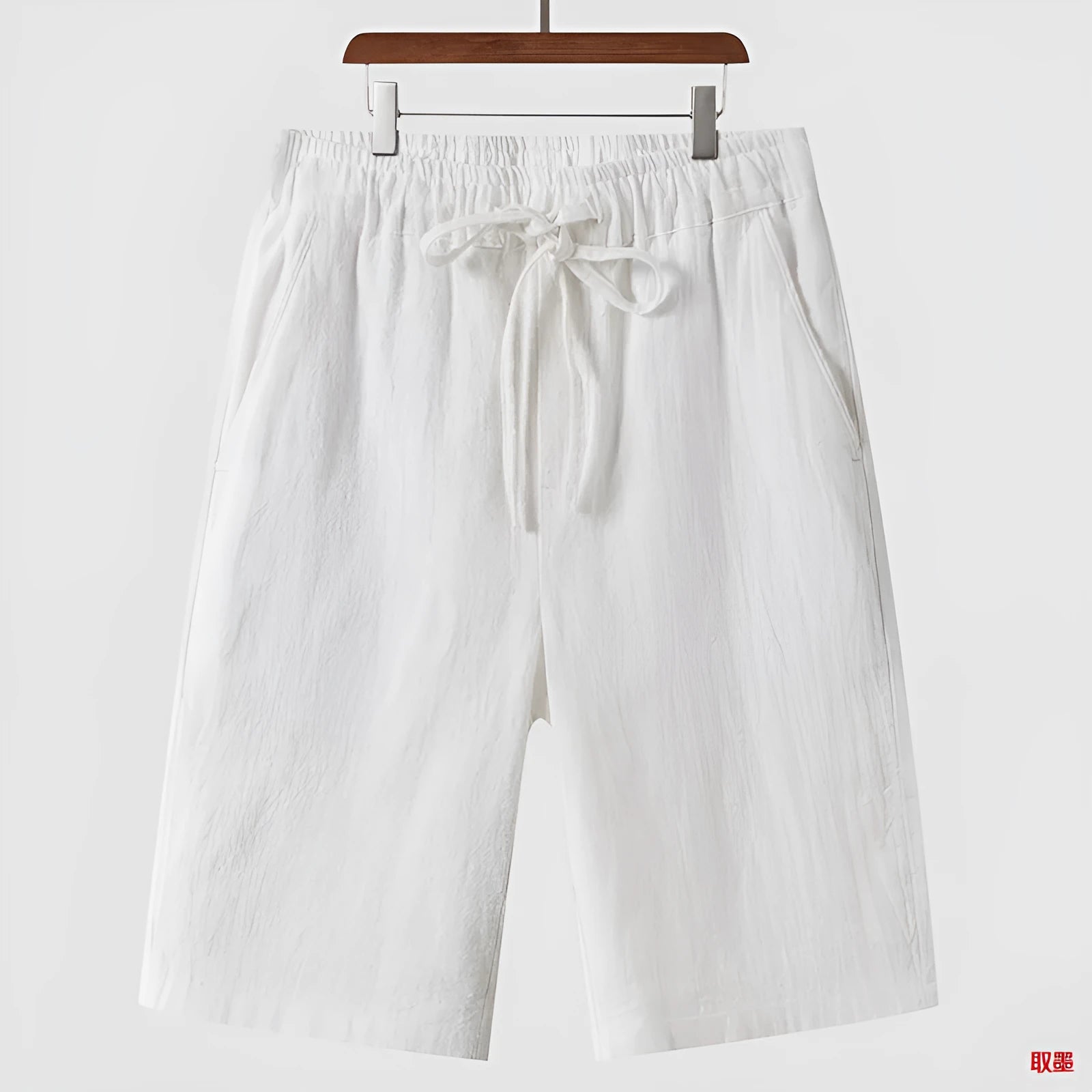 Men's beige linen casual shorts with loose cropped fit and elastic waistband laid flat