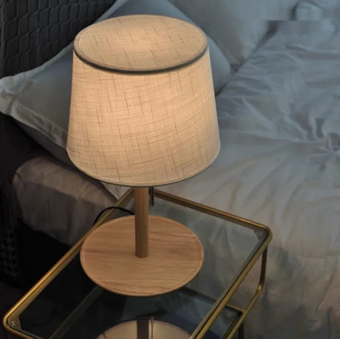 Walnut-coloured solid wood bedside lamp with white fabric shade on wooden table