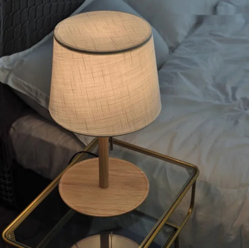 Walnut-coloured solid wood bedside lamp with white fabric shade on wooden table