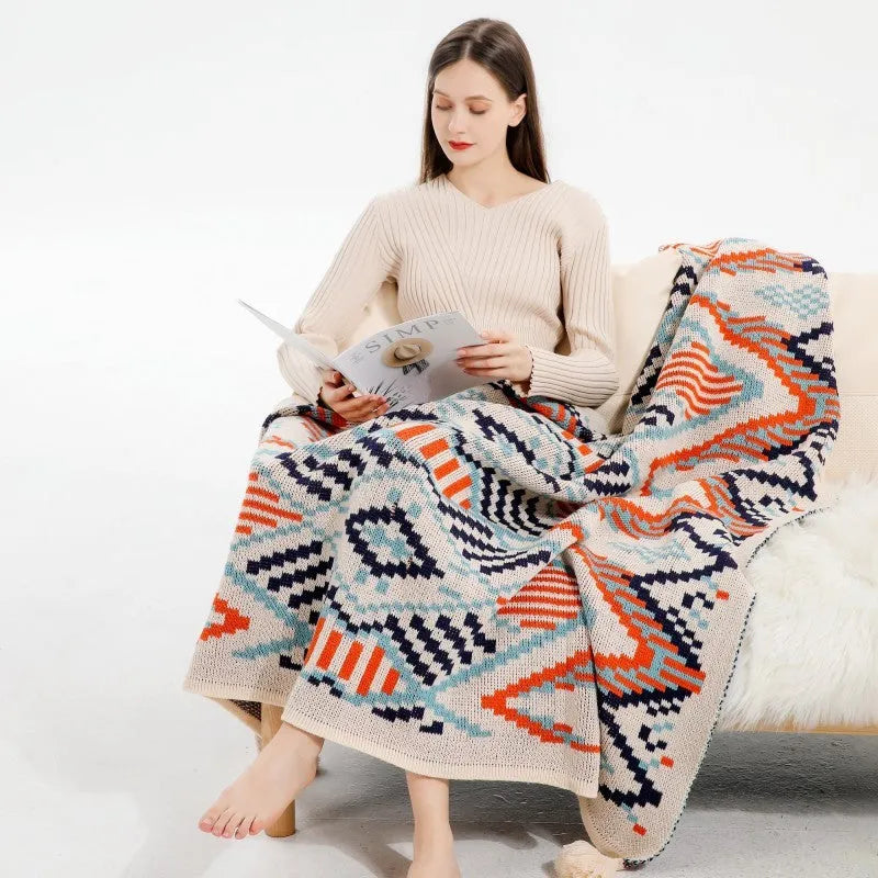 Beige and orange bohemian-style acrylic sofa blanket with tassel fringe on a grey sofa.