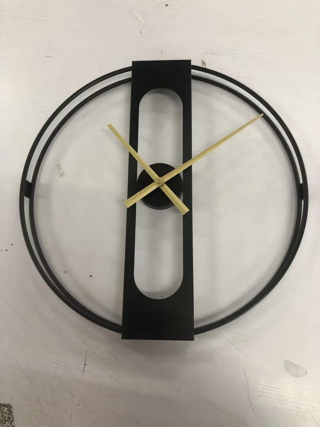 A large 50cm round metal wall clock on a wall, shown in black and gold colour variants.
