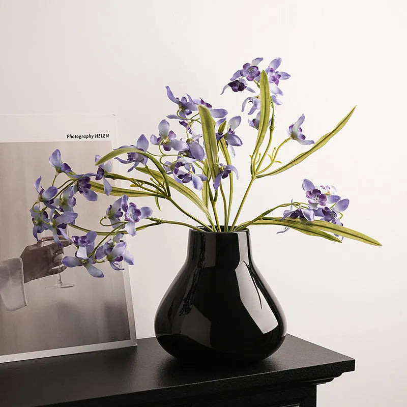 Ceramic round belly vase in black or white with artificial orchid stems on wooden surface