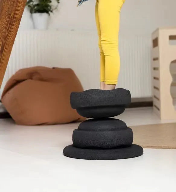 A plastic balance board for children, shown in mixed wood colour and solid black options.