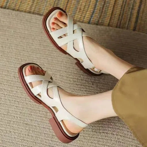 Women's black patent leather square toe sandals with cross straps on a low rubber sole.